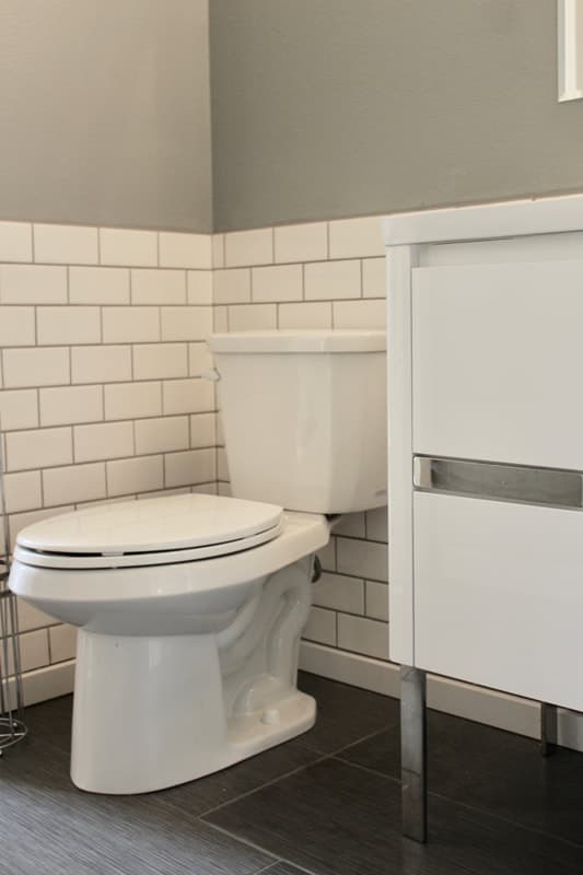 A completed bathroom remodel: a white toilet against white subway tile wainscoting, dark slate floor tile and a modern white floating vanity.