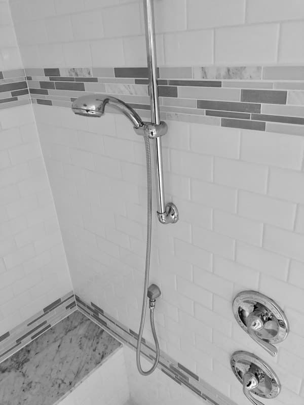 A shower remodel with white subway tile walls, a marble accent border and a chrome handheld showerhead on a slide bar.
