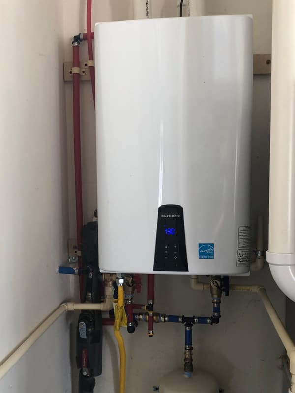 A Navien tankless water heater wall-mounted with neat copper and PEX pipe runs.