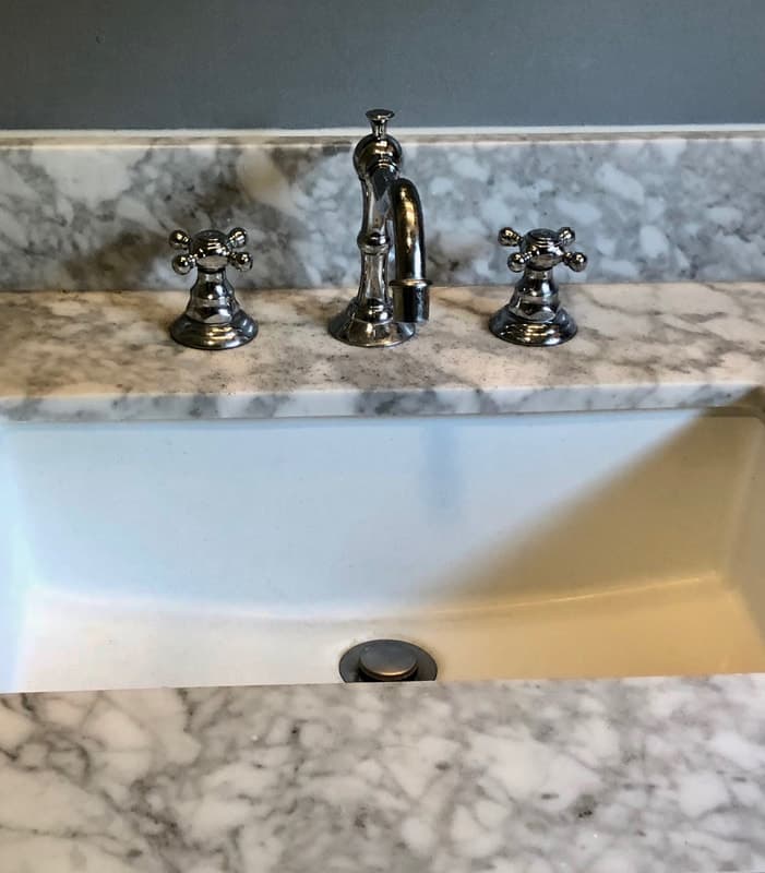An undermount sink with a vintage-style chrome cross-handle faucet on a Carrara marble vanity countertop.